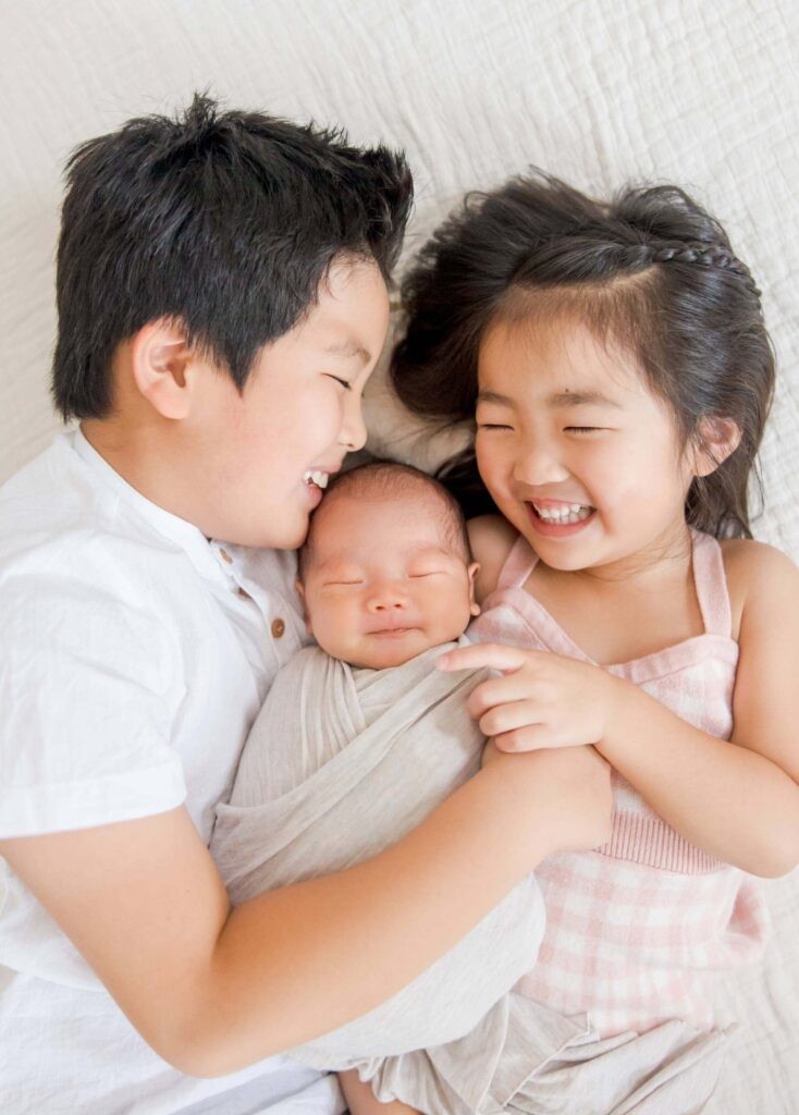 Two older siblings laughing while holding newborn brother