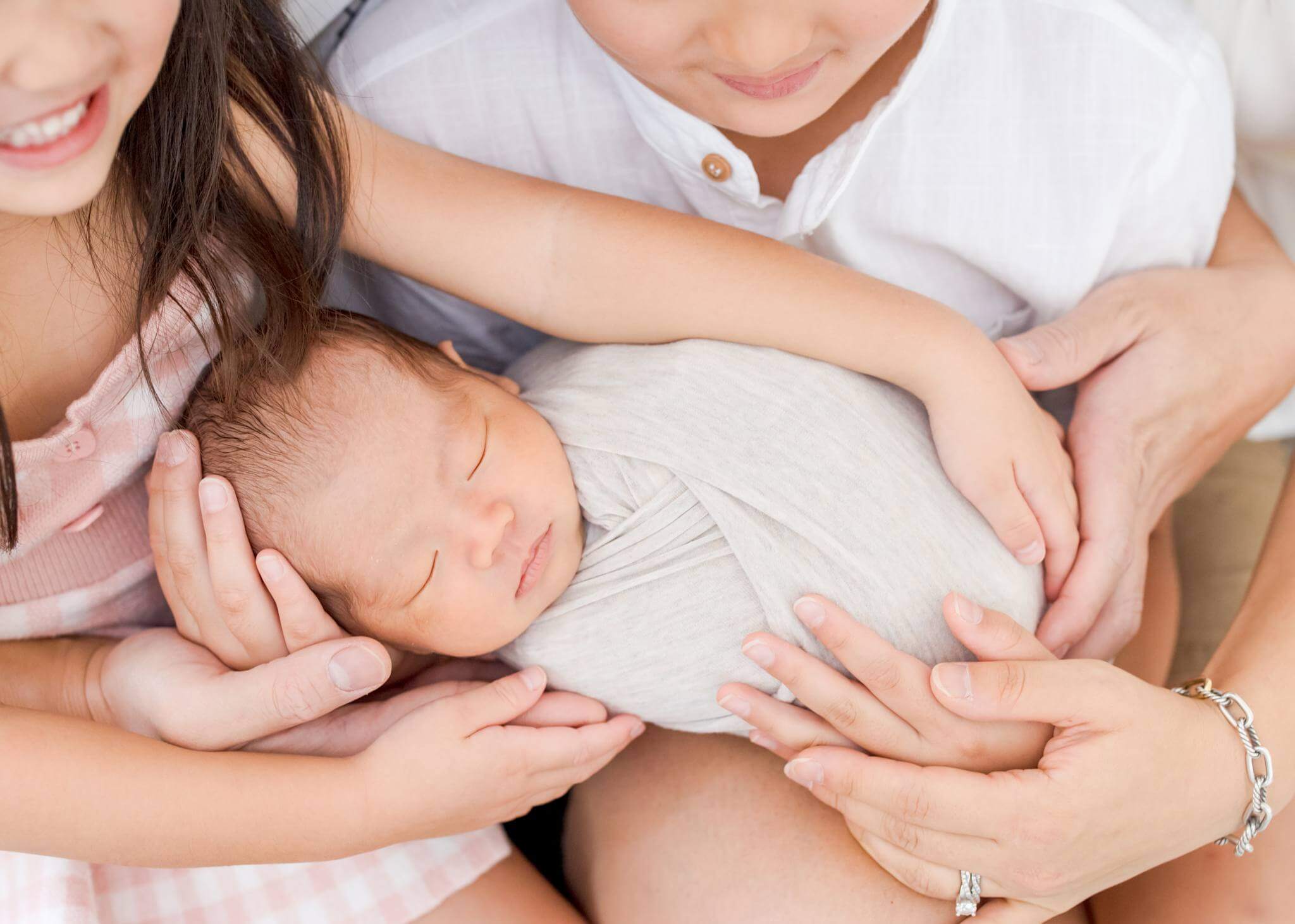 Family's hands touching newborn baby brother.