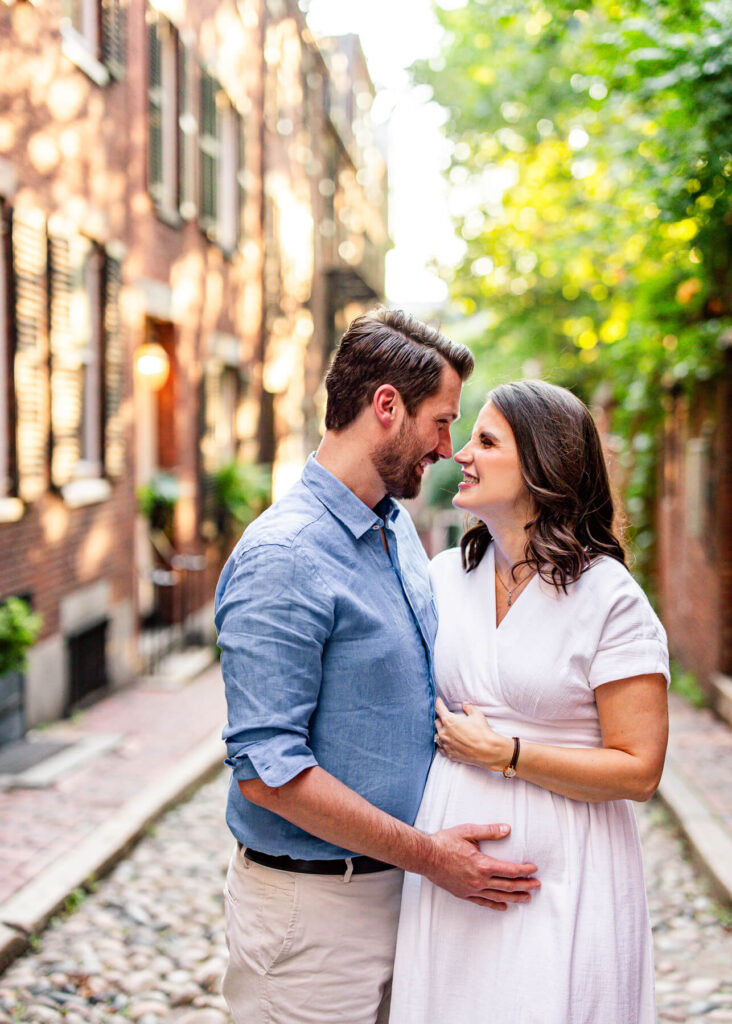 A couple looking at each other and smiling during a summer maternity photoshoot on Acorn Street in Boston.