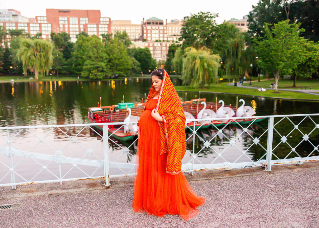An Indian mom wearing a traditional bright orange dress with the Boston swan boats in the backdrop.
