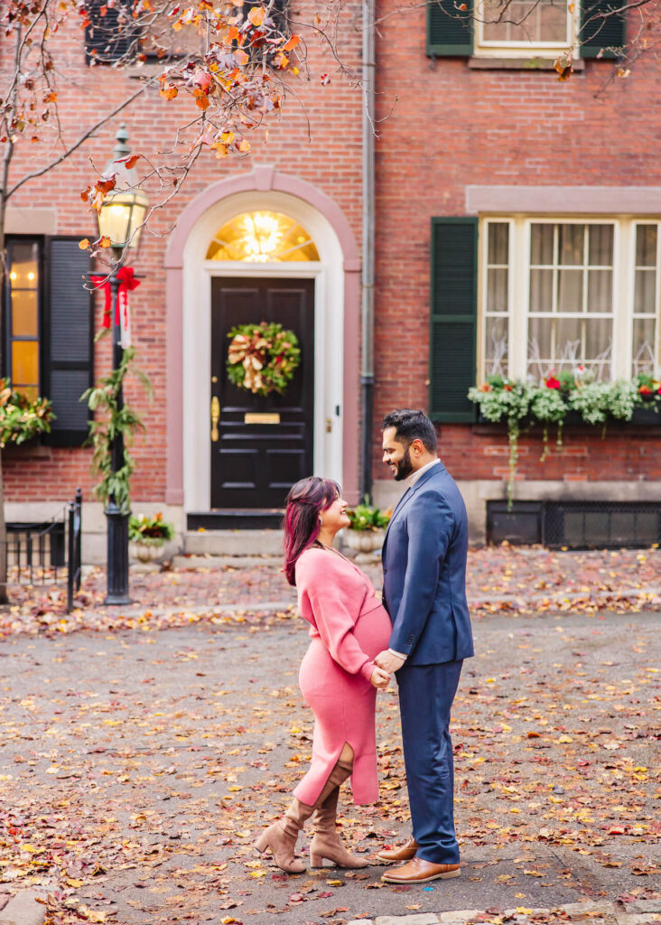 A pregnant couple during a fall photo session with the mom wearing a pink dress and the dad wearing a blue suit.