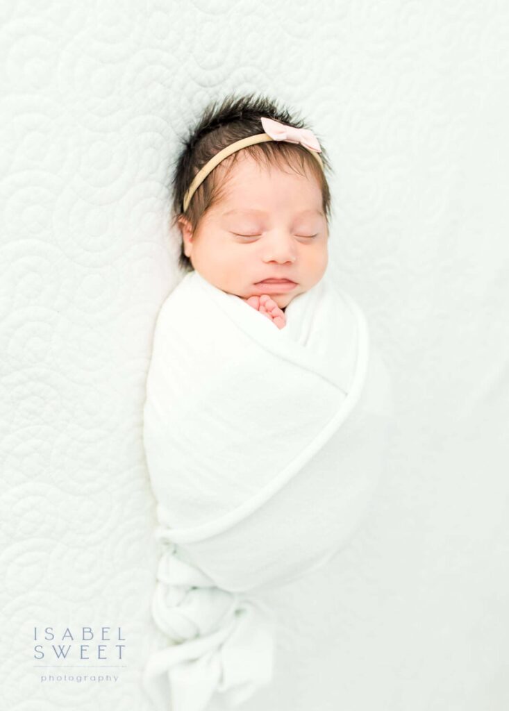 Newborn baby girl sleeping with a white wrap.