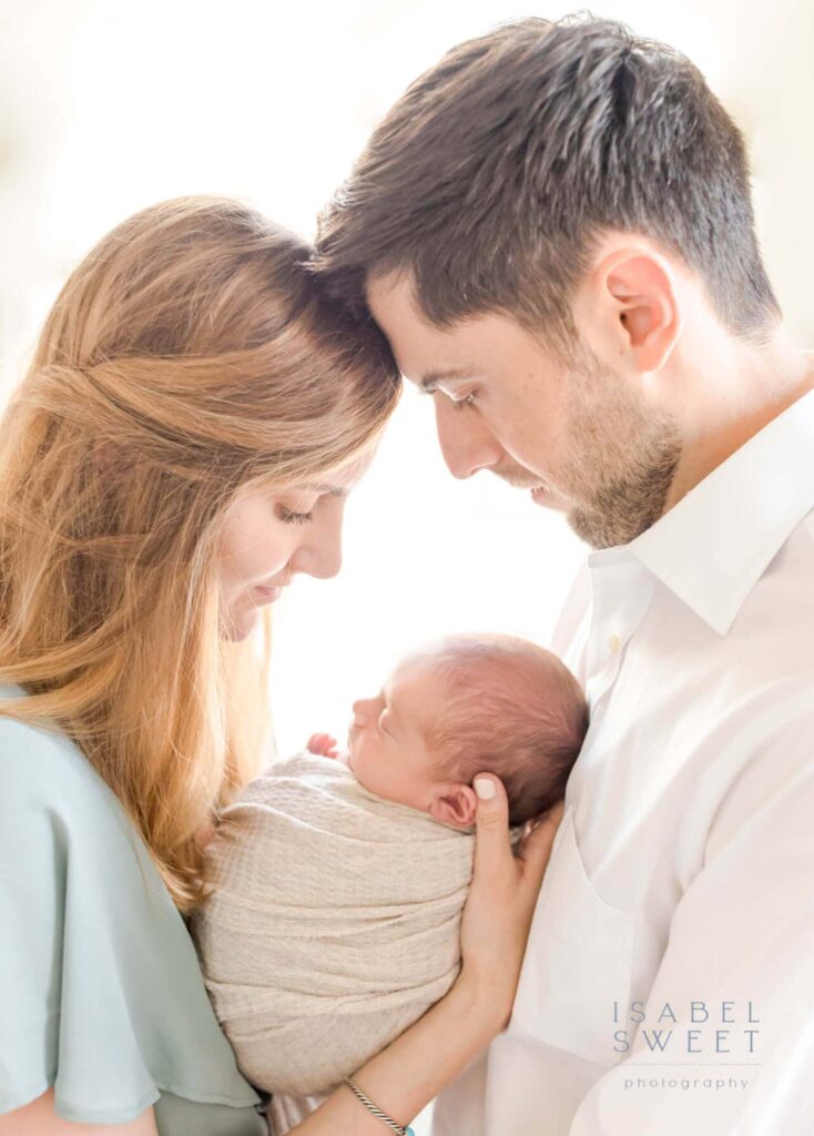 Profile image of a mom and dad touching foreheads and looking down at their newborn baby.